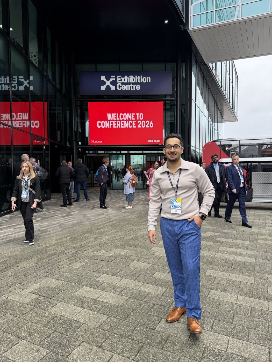 Dr Dev Gakhar outside the Exhibition Centre in Liverpool, under a red screen reading Welcome to Conference 2026, wearing a conference pass.